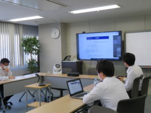 会議室のモニターに映した課題を見る日本コンピュータ開発の社員。