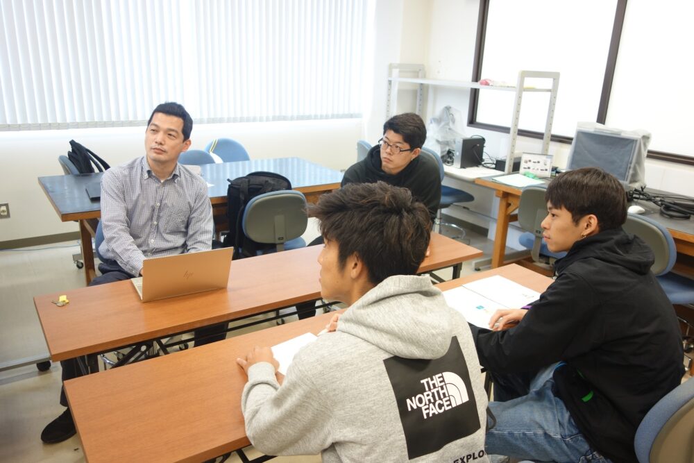 島名先生とその研究室の学生たち。
前方に注目しながら、ミーティングを行っている様子だろう。