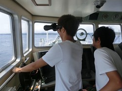 船内から、興味深そうに望遠鏡で海を眺める学生たち。
