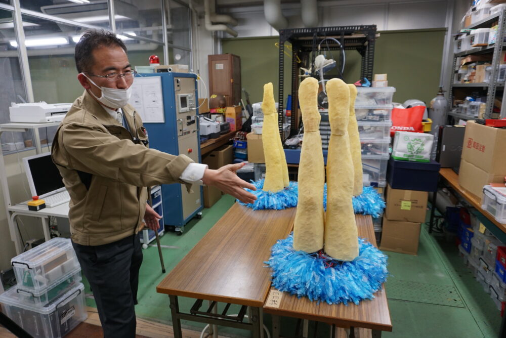 シンクロナイズドスイミングをモチーフにした2本の人の足のかたちをしたロボットの紹介をする田中先生。