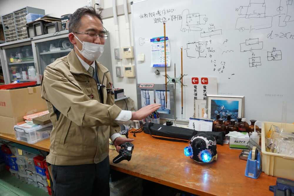 部分が光っているロボットを前に力説する田中先生。