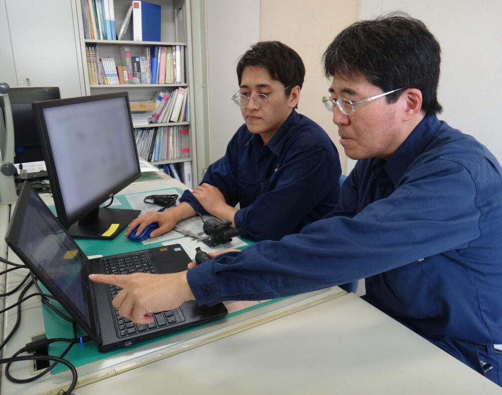 デスクの上で、PCをそれぞれ1台ずつ前に、山本さん、川村さんが打合せしている様子。