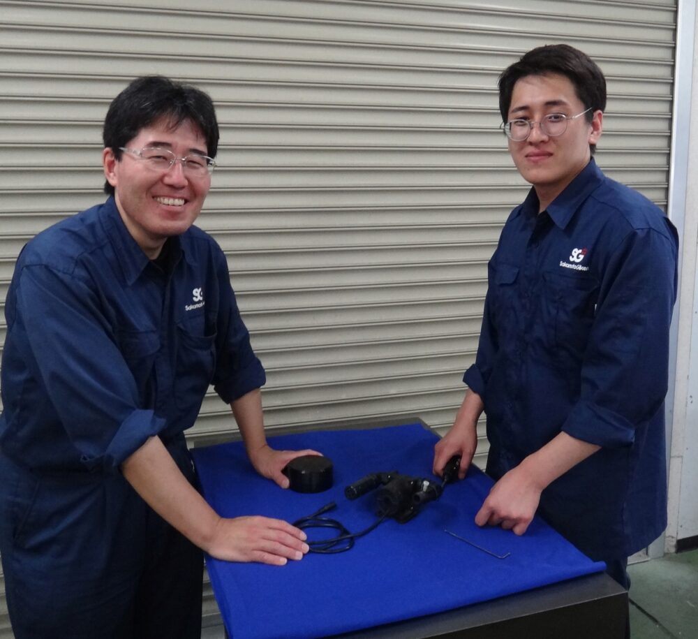 山本さんと川村さんが作業台を挟んで立っている。機器を組み立てている様子。