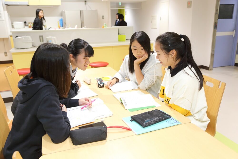 清潔な空間で、テーブルを囲んで、4人の学生が勉強しあっているところ。留学生に興味津々の様子。
