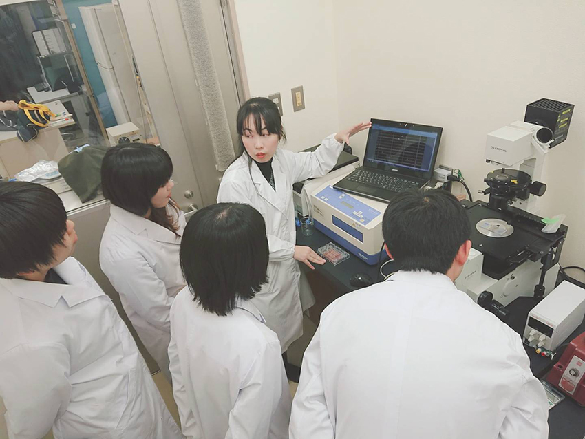 学生へ倒立顕微鏡を用いた実験についての説明する田頭先生。