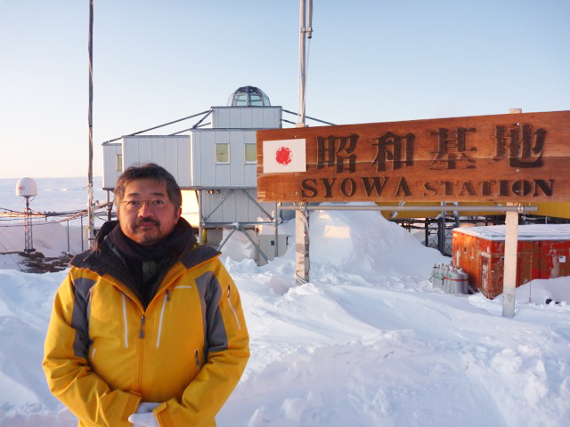 「昭和基地」と書かれた木製の看板の前で、防寒着を着こんで記念撮影をする岩波先生