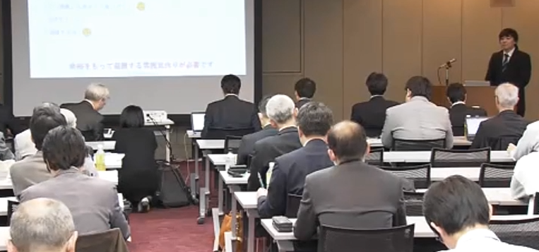 プロジェクターにスライドを映し、たくさんの受講者の前で発表する福田先生