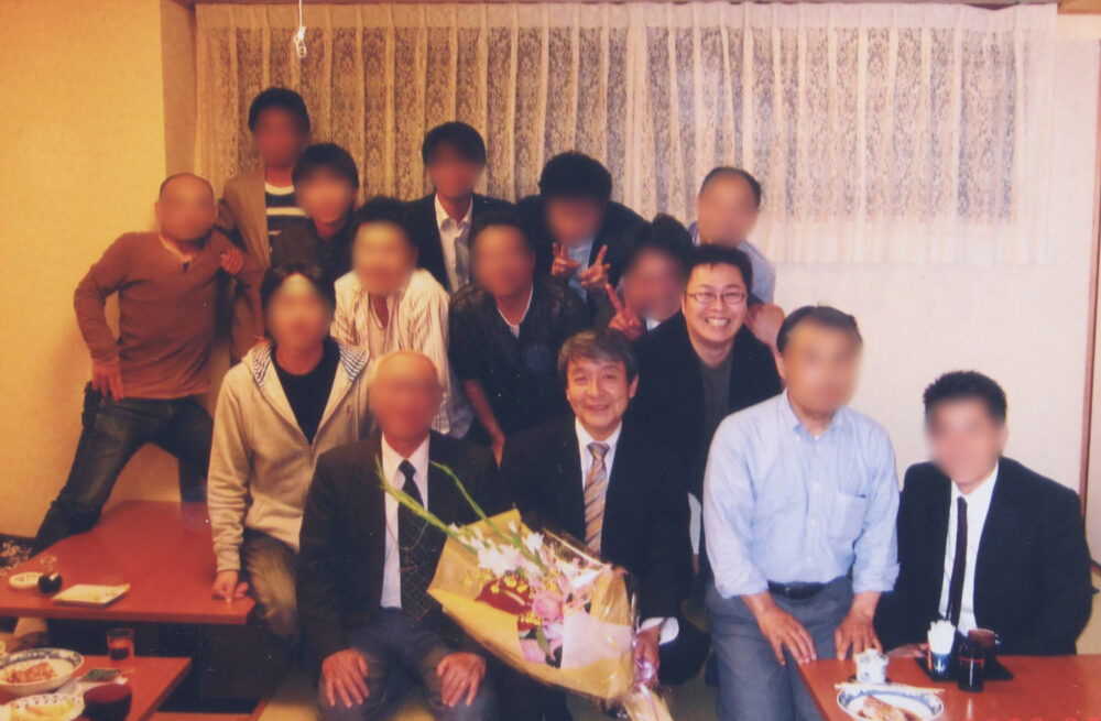 藤井先生が真ん中で花束を持ち、周りには関係者がたくさんいる集合写真