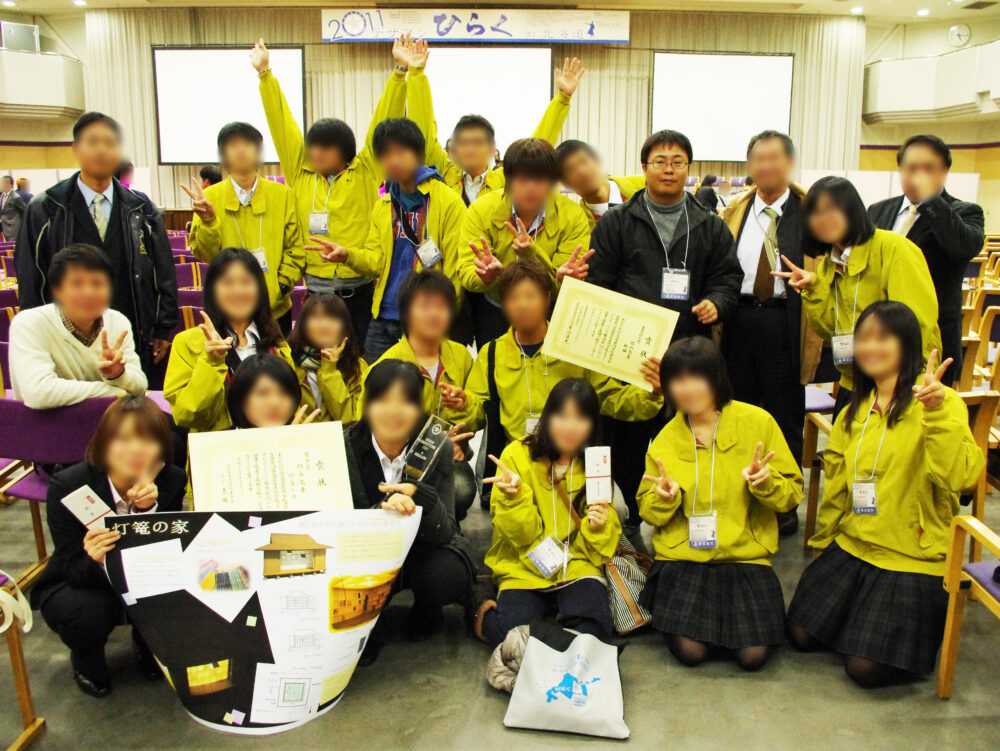 学生たちがからし色のおそろいのジャケットを着て、賞状を手に受賞記念写真