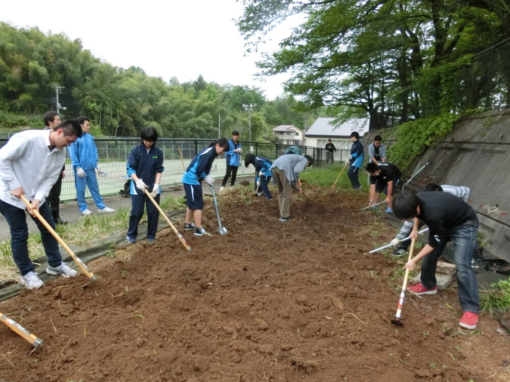 学生たちが鍬を持ち、土を耕している様子