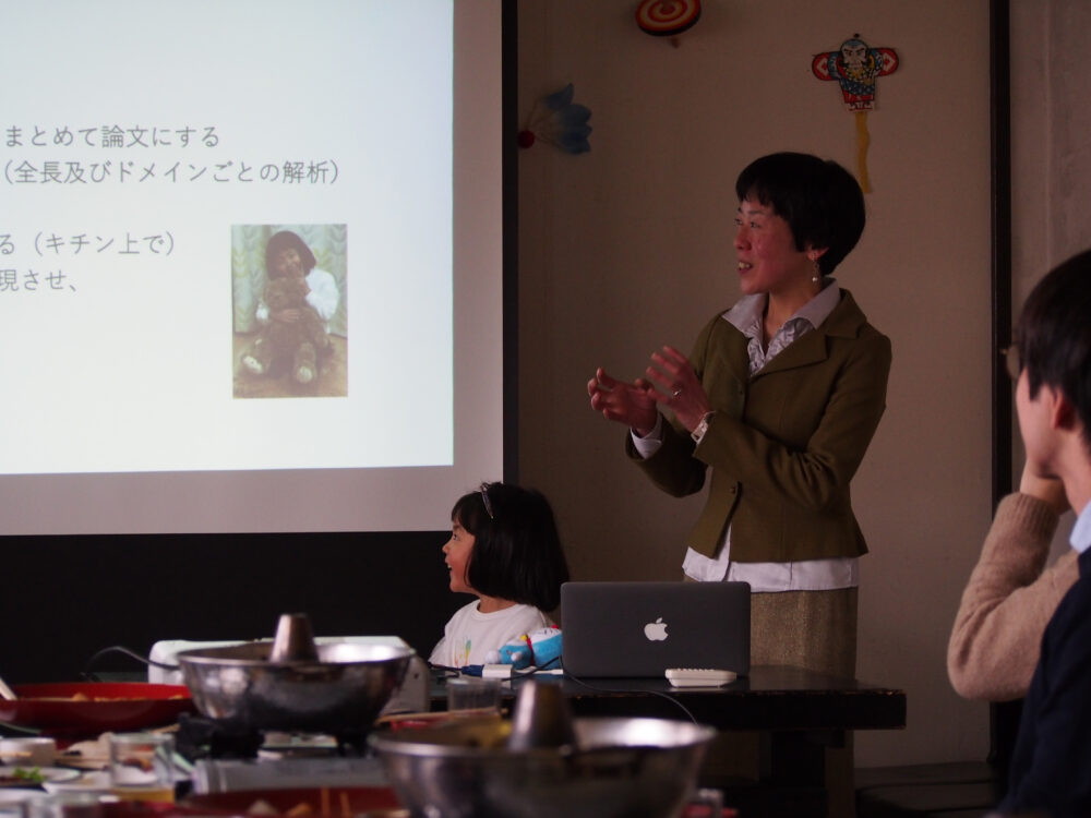 少し暗くした室内で、プロジェクターでスライドを映しながら、前のほうで話をする中川先生と、にこやかな娘さんの姿
