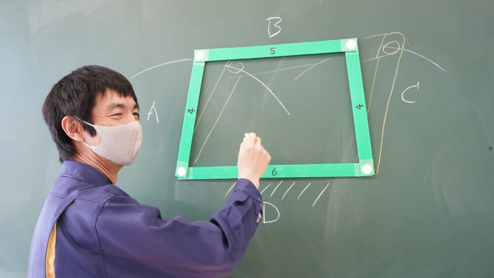 黒板に、緑の四角形（辺ABCD）を磁石でくっつけ、辺Dが固定されたときの、辺A・Cの動きをチョークで書き込む平澤先生
