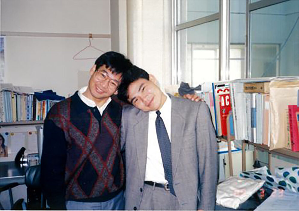 井田先生は大学時代のグレーのスーツを着た中武先生の肩に手を掛けている、2ショット写真