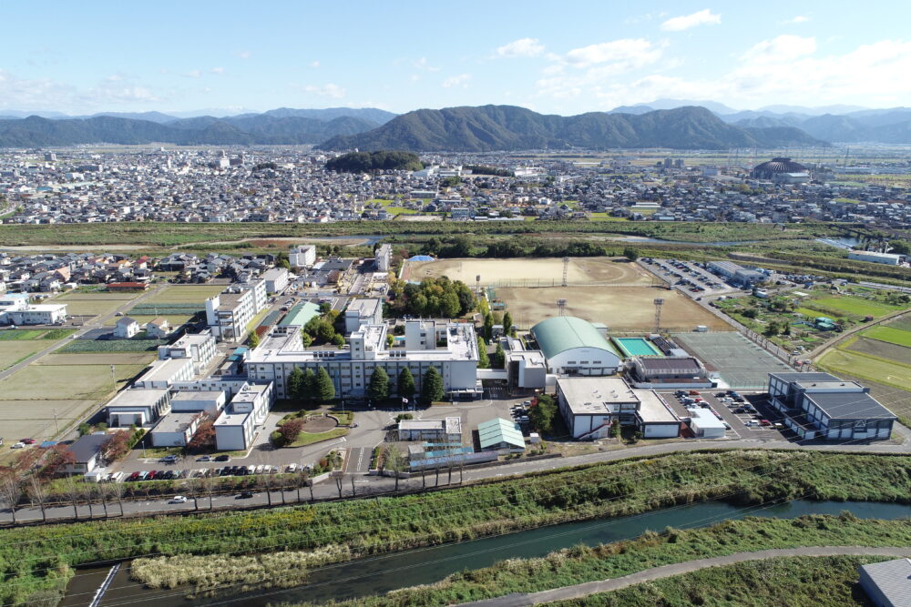 平野に住宅街が広がり、緑に囲まれて白い校舎が連なる福井高専の空撮