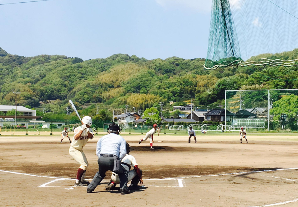 土のグラウンドで野球をプレーする学生たち