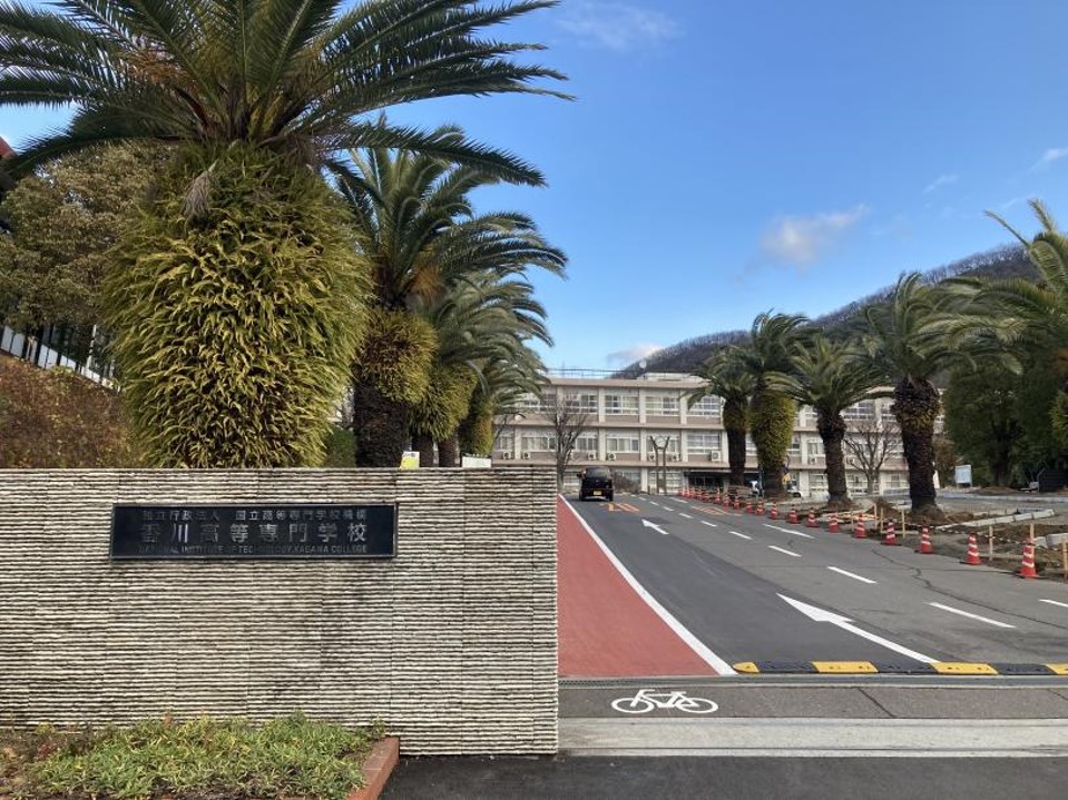 香川高専高松キャンパスの正門から校舎を写した写真。
南国風の低木が一定の間隔で植栽されている