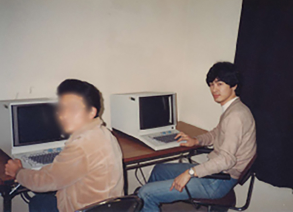 大きな箱型の計算機に向かって実験を行う学生時代の古内先生