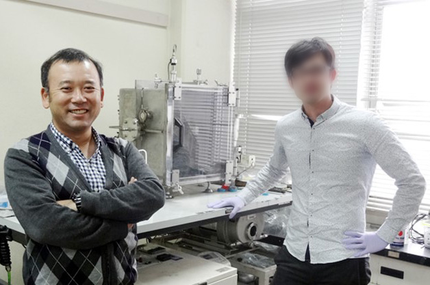 研究室にて、学生とともに、腕を組み笑顔の稲田先生