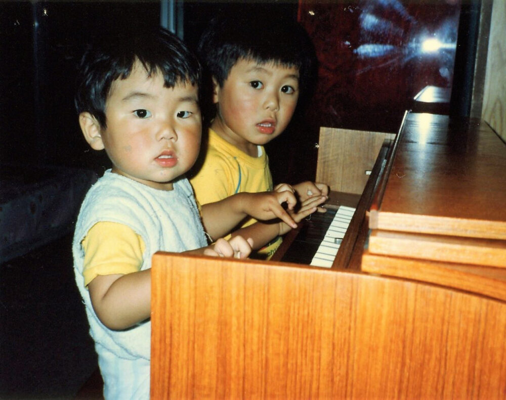 幼顔の弟さんと、チェンバロの鍵盤を指先で押す、幼少期の冨沢先生