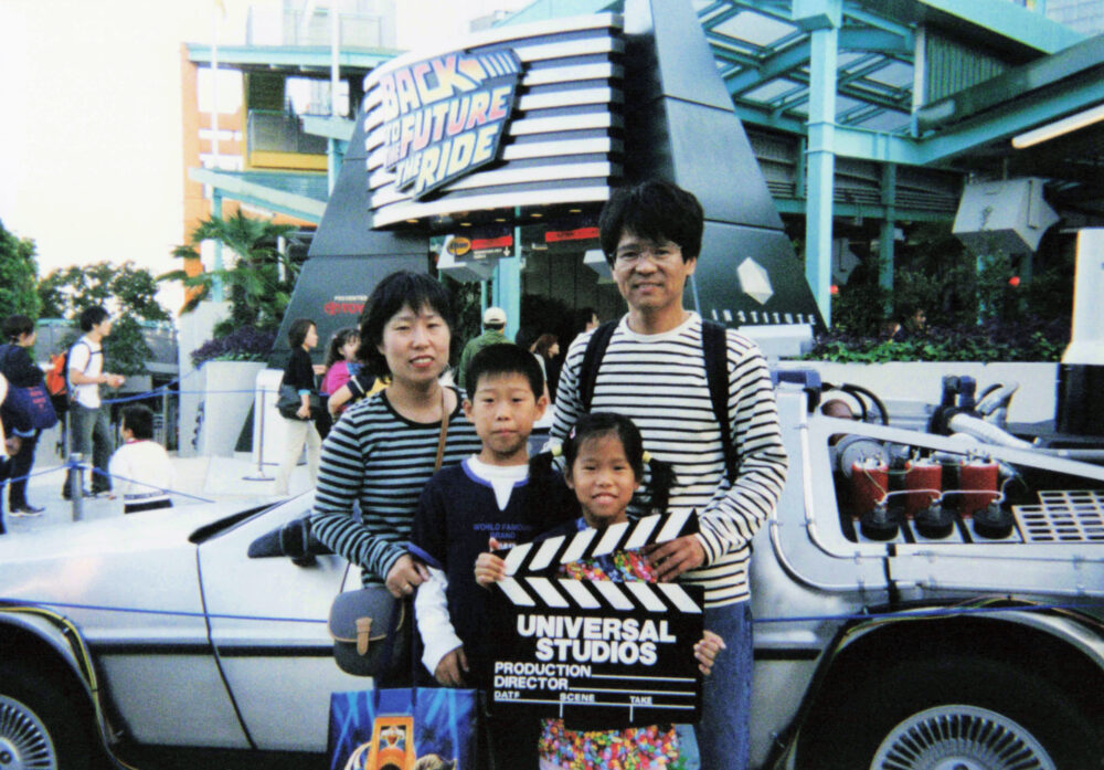 バックトゥザフューチャーのデロリアンを背景に、家族で写真を撮る、奨学生時代の梶原先生