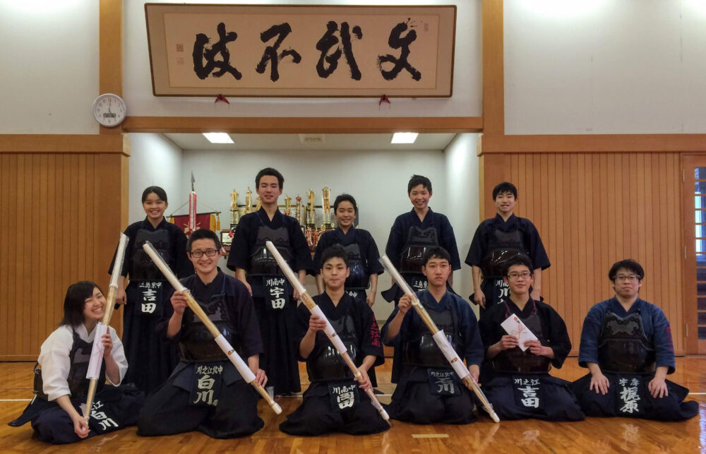 武道場で、剣道着を着て、学生らとともに集合写真