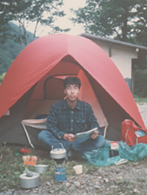 屋外、キャンプ場にて、赤いテントを張り、炊事をする、学生時代の山田先生