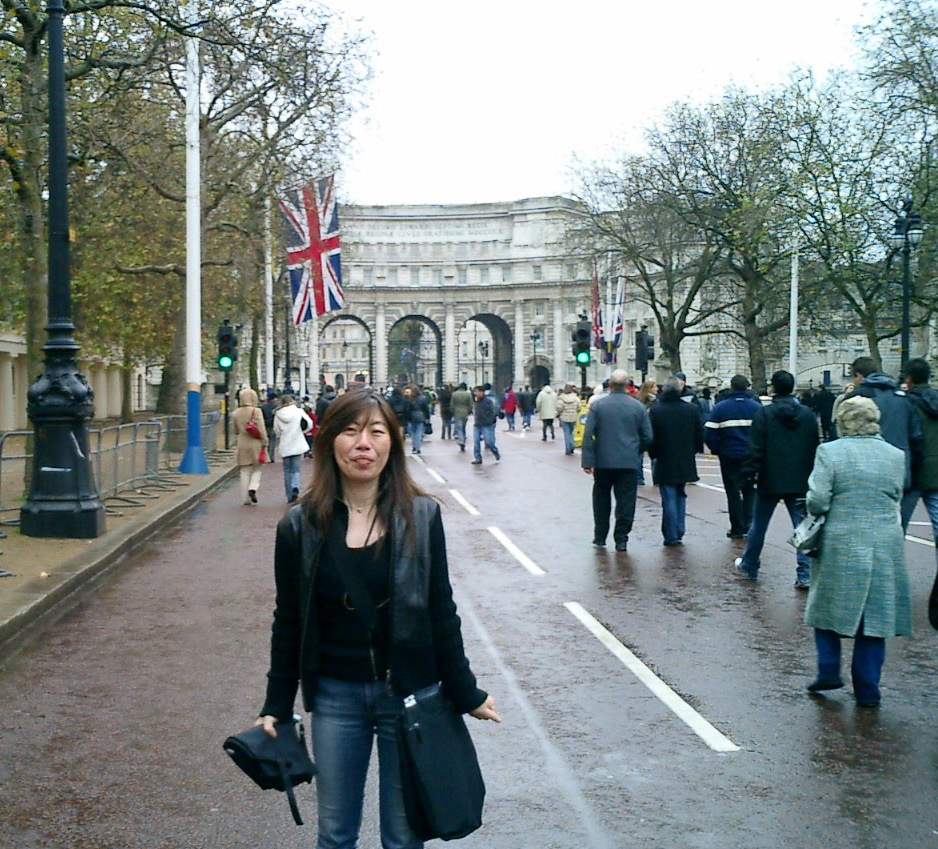 イギリス国旗が飾られ、背景には白い城門。曇天の、少し水たまりのある道を人々が行き交っている