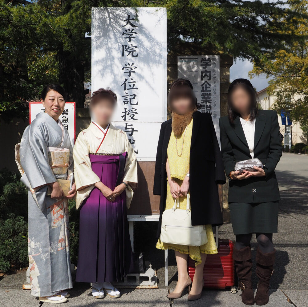 4名の女性が正装して、正門で記念撮影