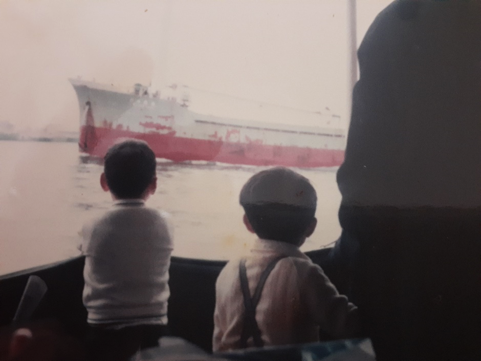海上を進む、上下の塗装が赤と白の船を見つめる。幼少期の奥村先生