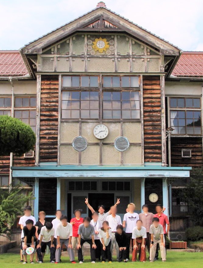 古い木造校舎の前で写真に写る光井先生と学生のみなさま