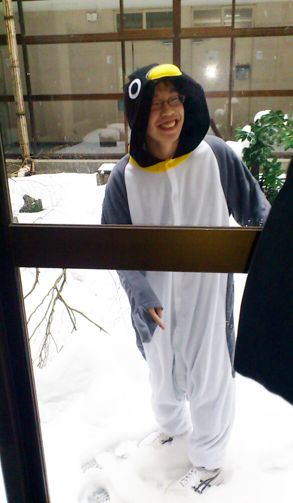 雪景色の中、ペンギンの着ぐるみを着て微笑む任田先生