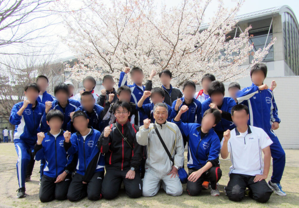 満開の桜の前で写真に写る光井先生と谷岡先生と、陸上競技部のみなさま