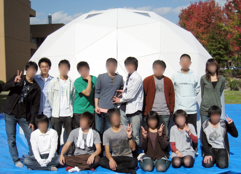 白くて丸いドーム状の建物の前で写真に写る光井先生と、研究室のみなさま