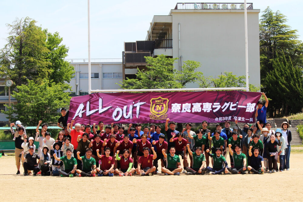 「ALL OUT 奈良高専ラグビー部」と書かれた横断幕の前で写真をとる生徒・OBの皆さん