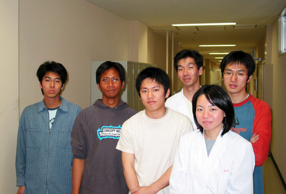 廊下で飯島研究室のみなさまと並んで写真に写る飯島先生