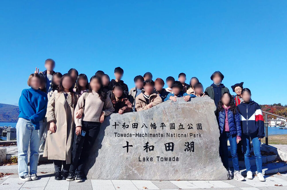 十和田湖で並んで写真に写る横田先生と学生の皆さま