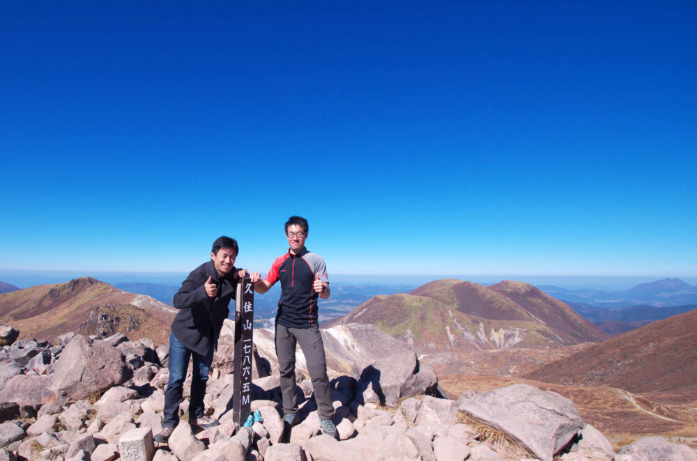 山頂で青空の下、写真に写る藤本先生