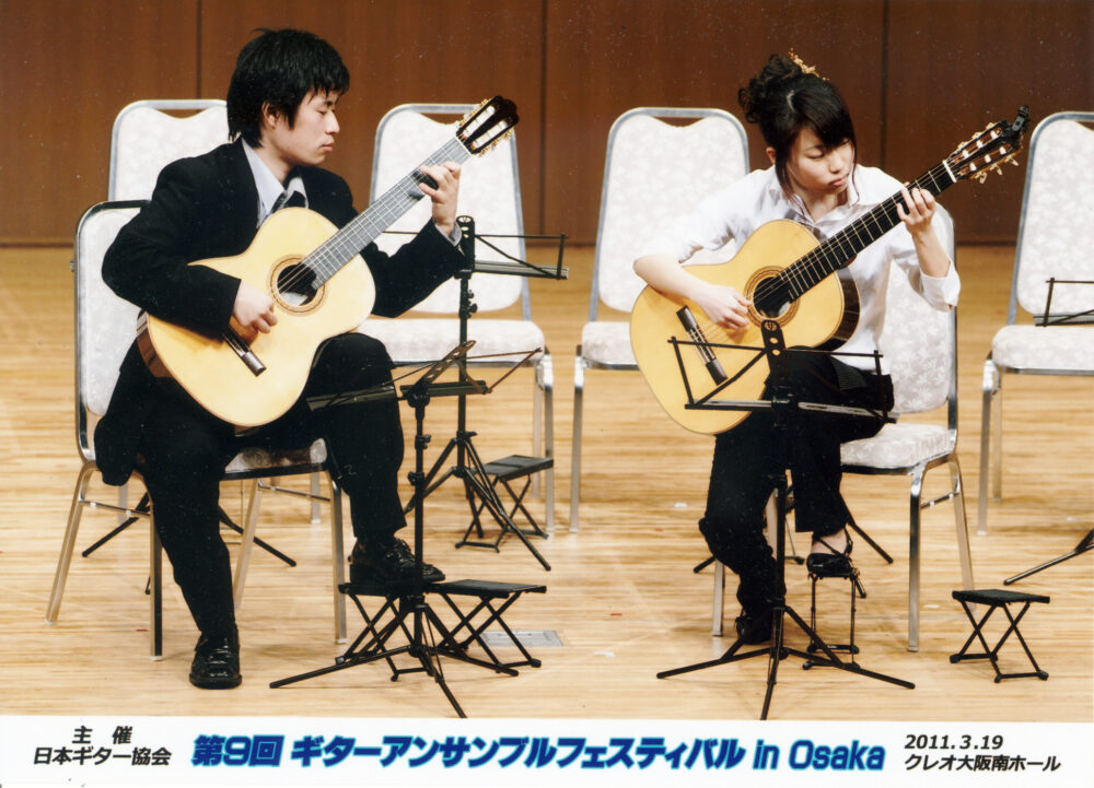 スーツを着てギターを弾く藤本先生と奥様