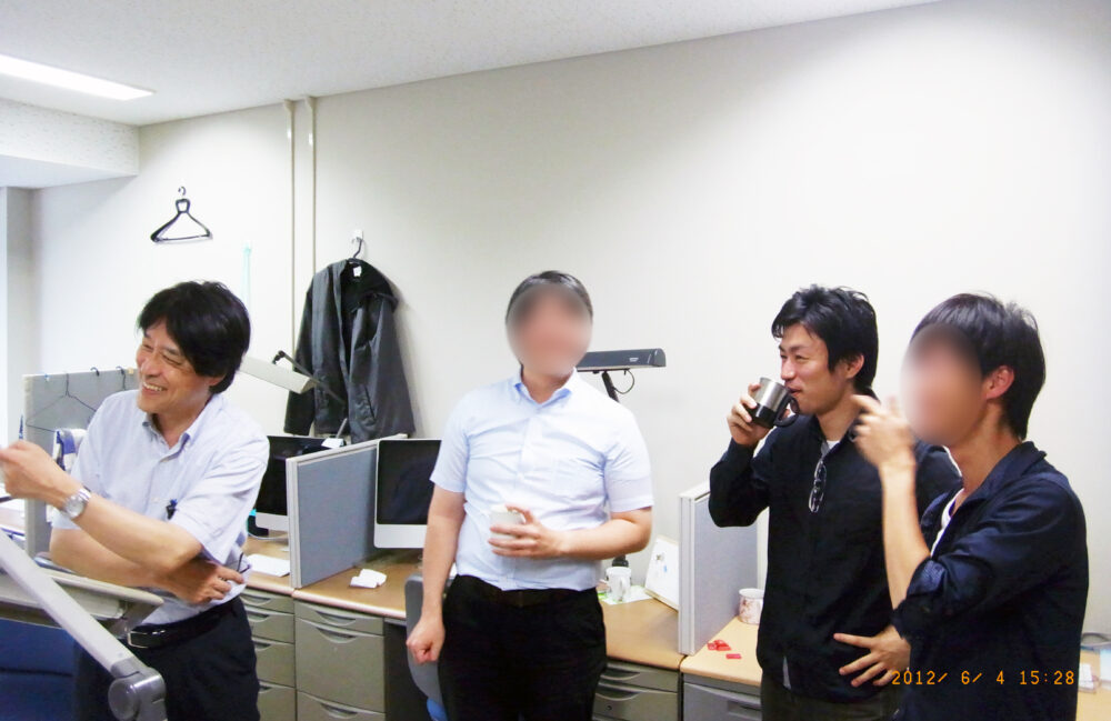 研究室で、先生と学生と笑顔で議論をされている藤本先生