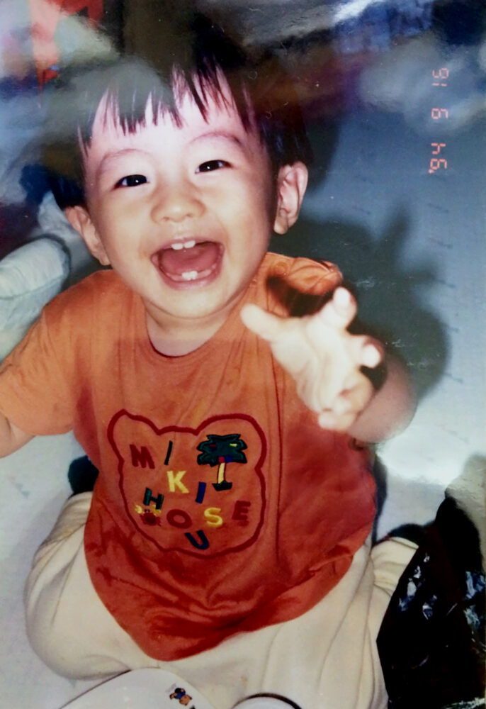 カメラに向かって笑顔を見せる、幼少期の冨田さん
