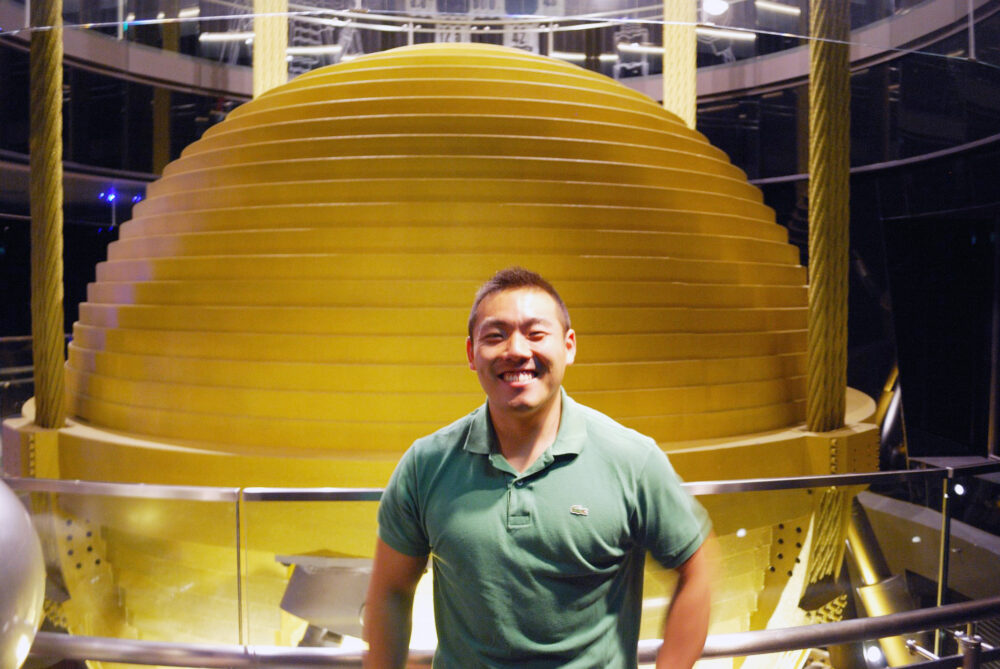 黄色くて丸い巨大なダンパーの前で、笑顔で写真に写る小川先生