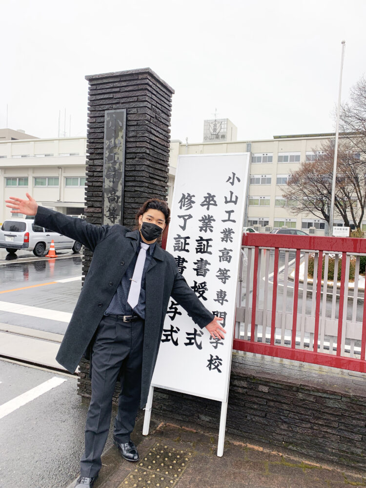 小山高専の門の前で記念写真を撮る中嶋さん