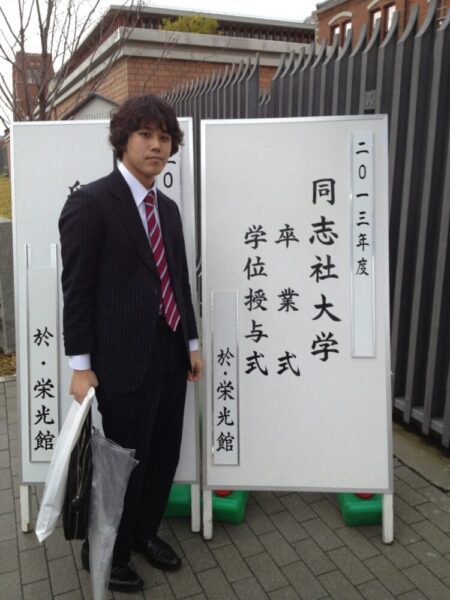 同志社大学の卒業式で、立て看板の前に立つ石井先生