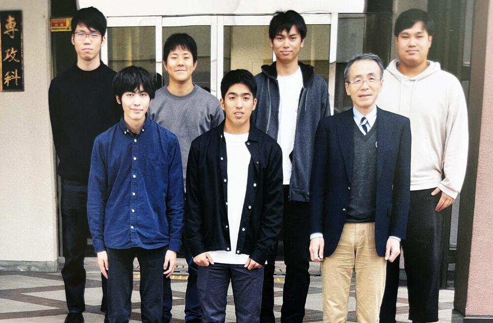 専攻科の入口の前で写真に写る高田先生と学生のみなさま