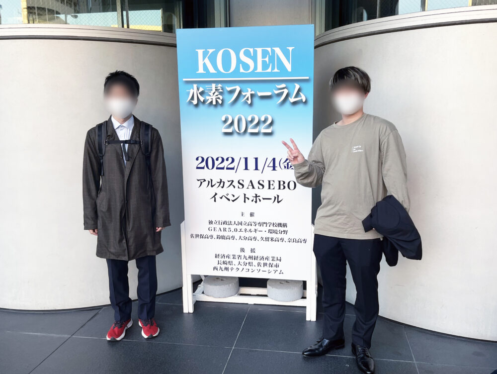 KOSEN水素フォーラム2022の看板の前で写真に写る学生さん２人