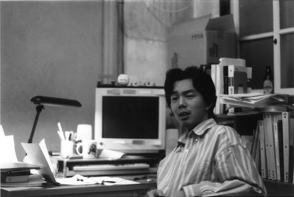 学生時代（博士課程在学中）、大阪府立大学の研究室にて。モノクロ写真。座ってこっちを見ている衣笠先生。
