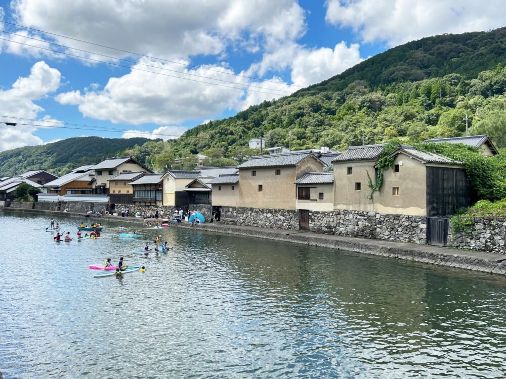 自然に囲まれた美しい佐用町平福の町なみ。手前の川ではカヌーをしている人々が映っている。