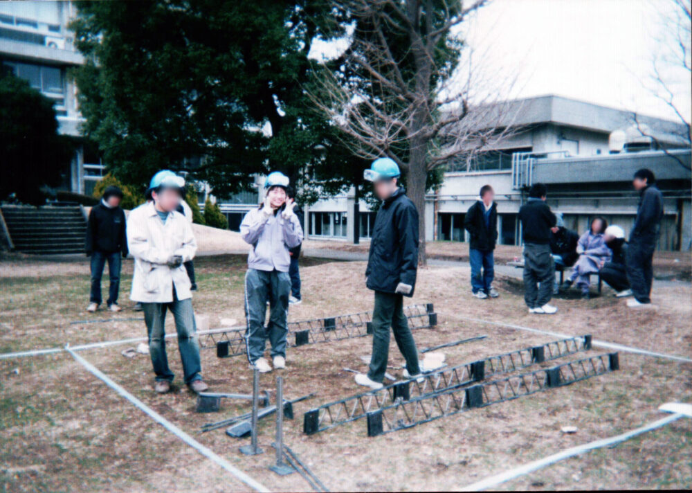 ヘルメットと作業着で、他の学生の皆さんと作業をする小田先生