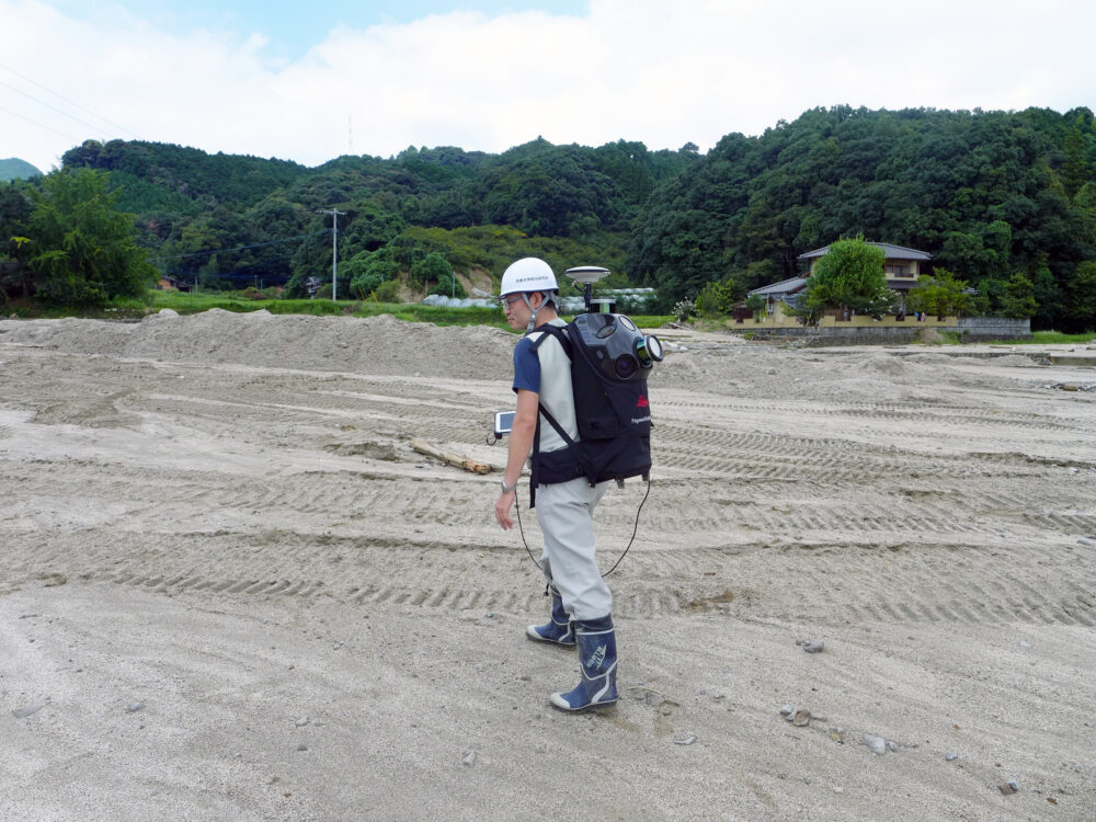 大きな黒いリュックを背負い、ヘルメットをかぶって調査をする佐山先生