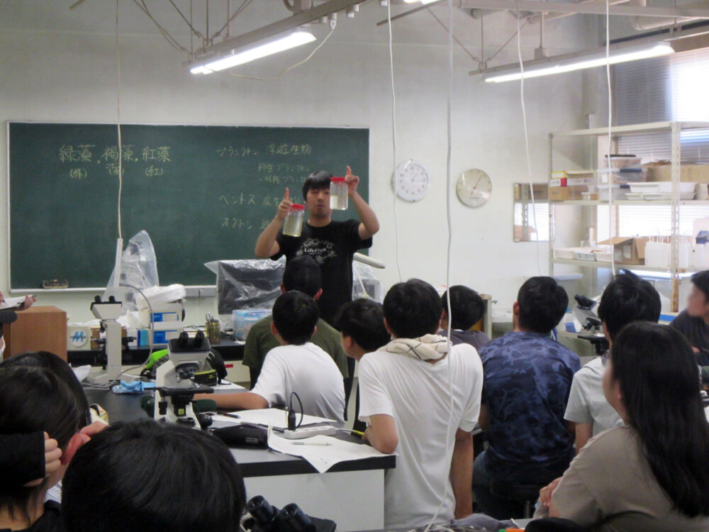 盈進学園 盈進中学高等学校の生物部を対象にプランクトンの観察実習を行う近藤先生。教壇に立ってそれを学生が聞いている様子